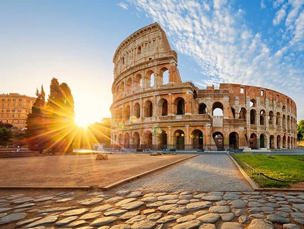 The Colosseum in Rome at sunrise with sun rays shining brightly.