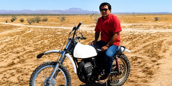 Man in red shirt sitting on a dirt bike in a desert.