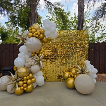 Gold and white balloon arch with a gold sequin backdrop outdoors.