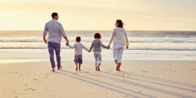 Family of four holding hands and walking on the beach at sunset.