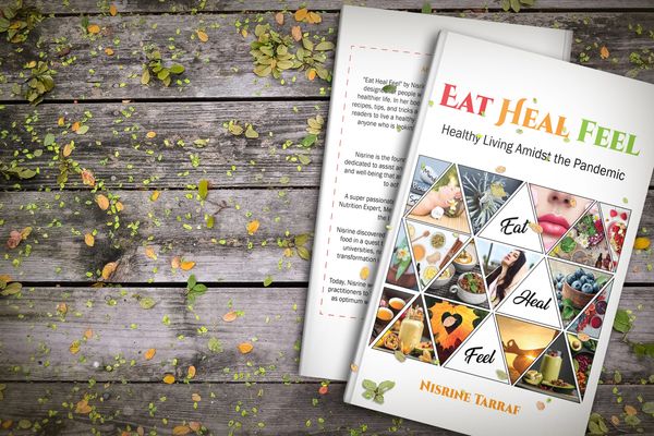 Book titled 'Eat Heal Feel' on healthy living during the pandemic, placed on a wooden surface with scattered leaves.