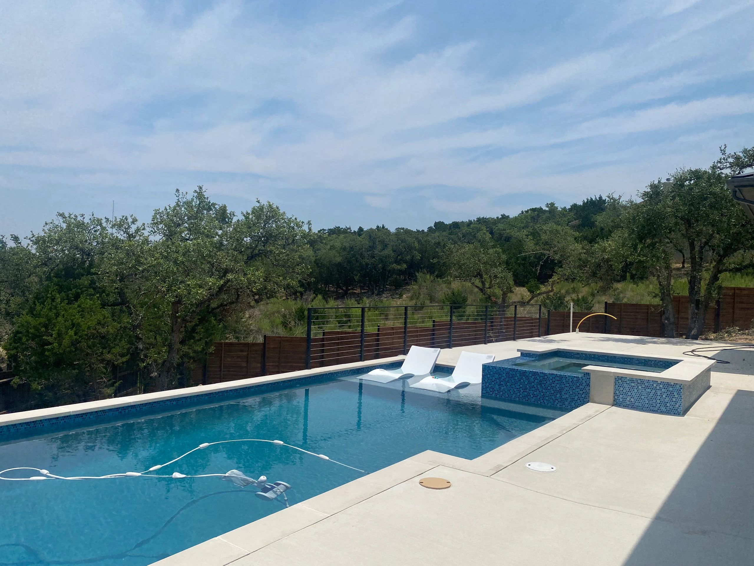 Modern pool with spa and loungers surrounded by nature.