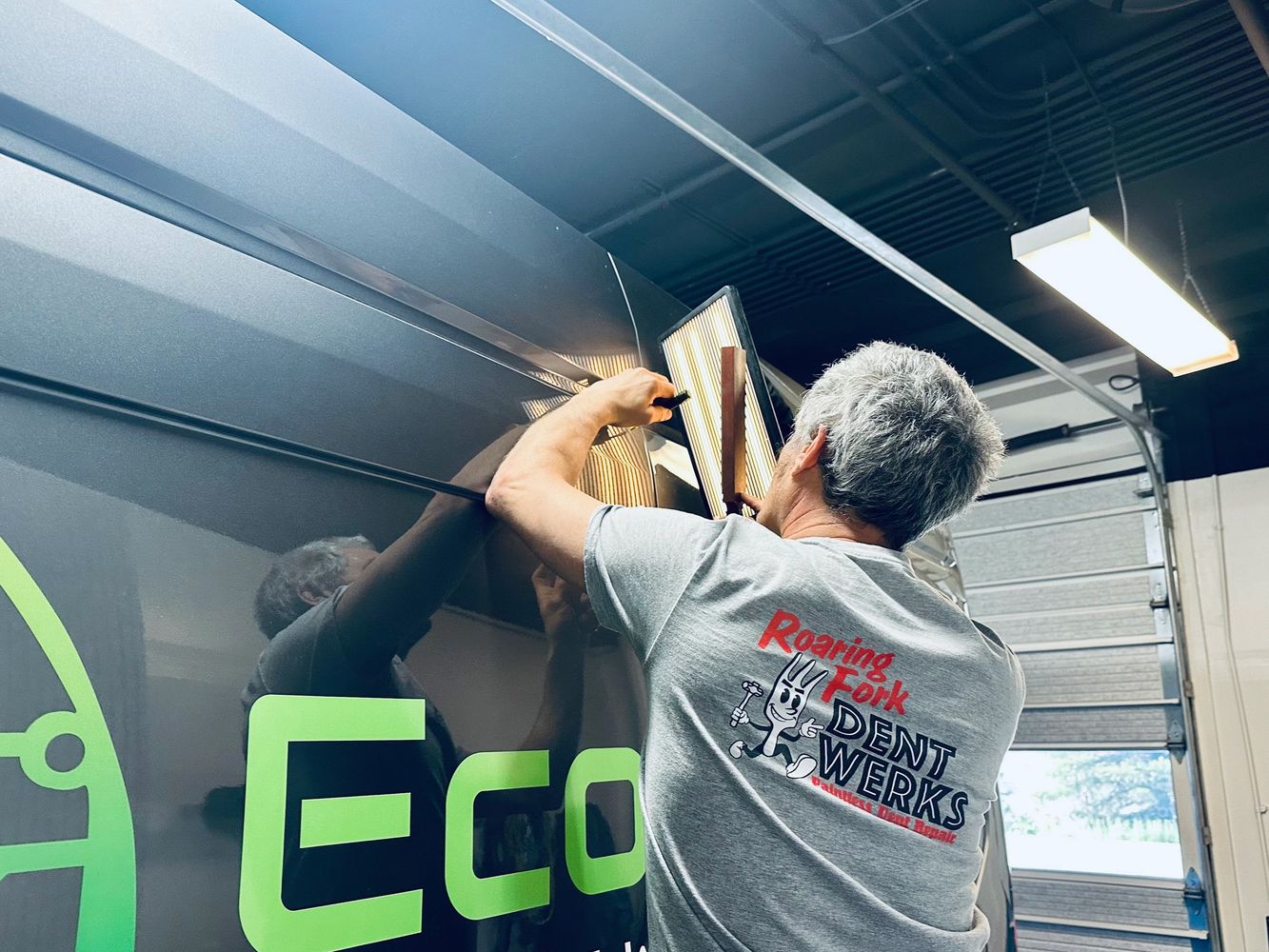 A man repairs a dent on a vehicle in a garage.