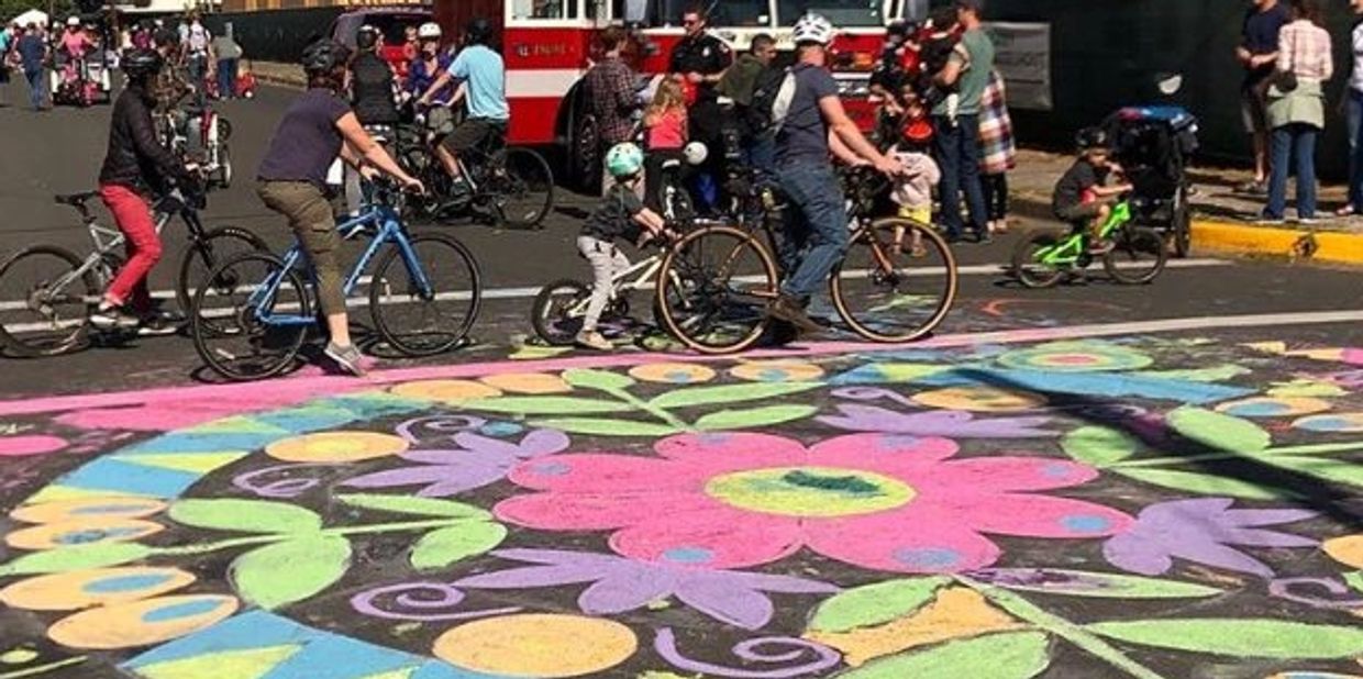People of all ages riding bikes on a street with colorful floral chalk art.