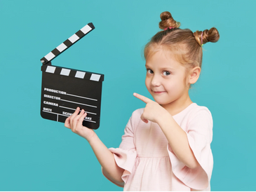 A young girl holding and pointing at a film clapperboard.