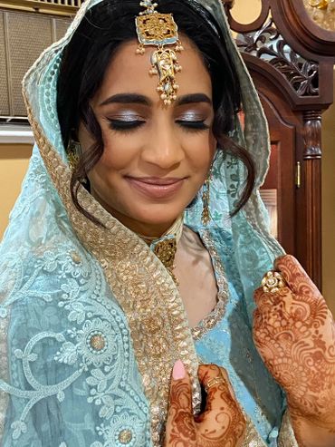 A bride in traditional attire with henna designs on her hands and a serene smile.