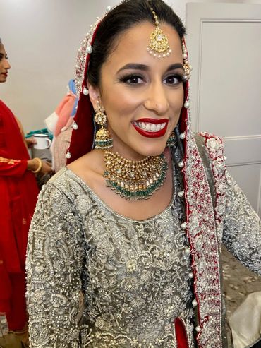 Smiling bride in traditional South Asian wedding attire with intricate jewelry and embroidery.