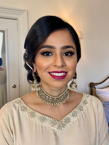 A smiling woman wearing traditional jewelry and elegant makeup.