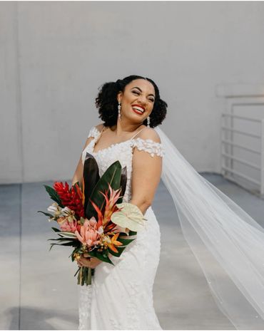 Joyful bride in white dress holding vibrant tropical bouquet.