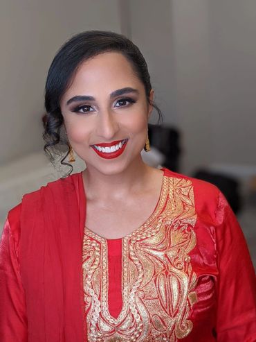 A smiling woman in a red and gold traditional outfit with elegant makeup.