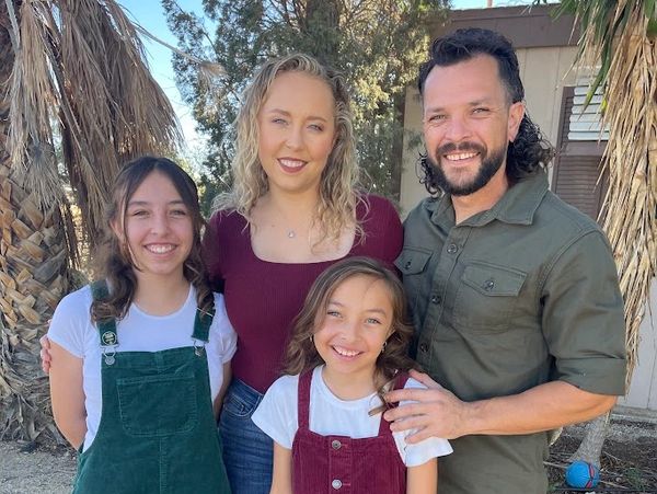 Smiling family of four posing outdoors near palm trees.