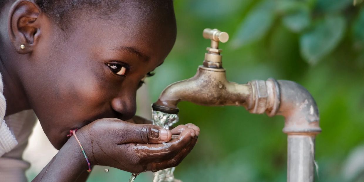 Black/African or African American girl drinking water from a faucet with cupped hands.