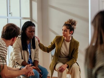 4 people sitting in a circle. A female puts her hand on another's shoulder in support