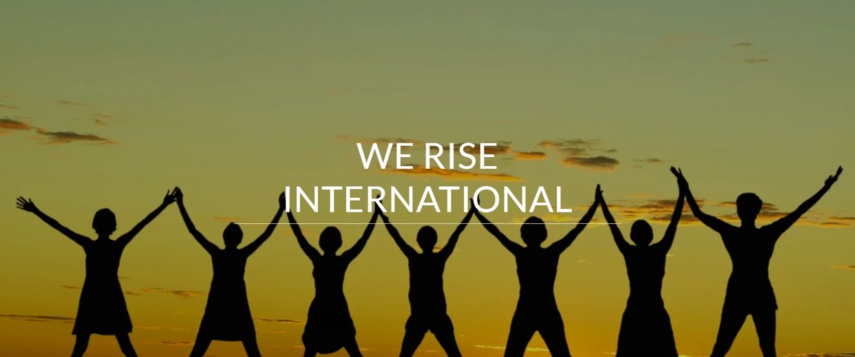 People with hands linked and raised to the sky in front of a sunset. 