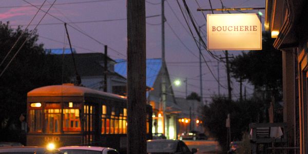 Evening street scene with a lit streetcar and a glowing Boucherie sign.