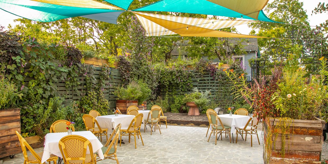 Cozy outdoor dining area with shaded tables and lush greenery.