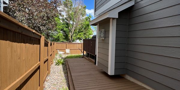 Wooden deck and fence along house with trees in background.