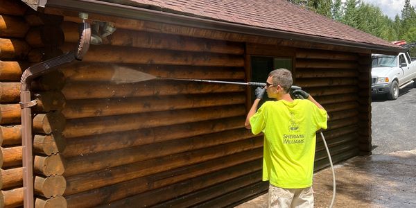 Man pressure washing a wooden cabin exterior.