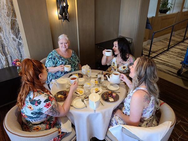 Four women enjoy tea and desserts around a round table in a cozy setting.
