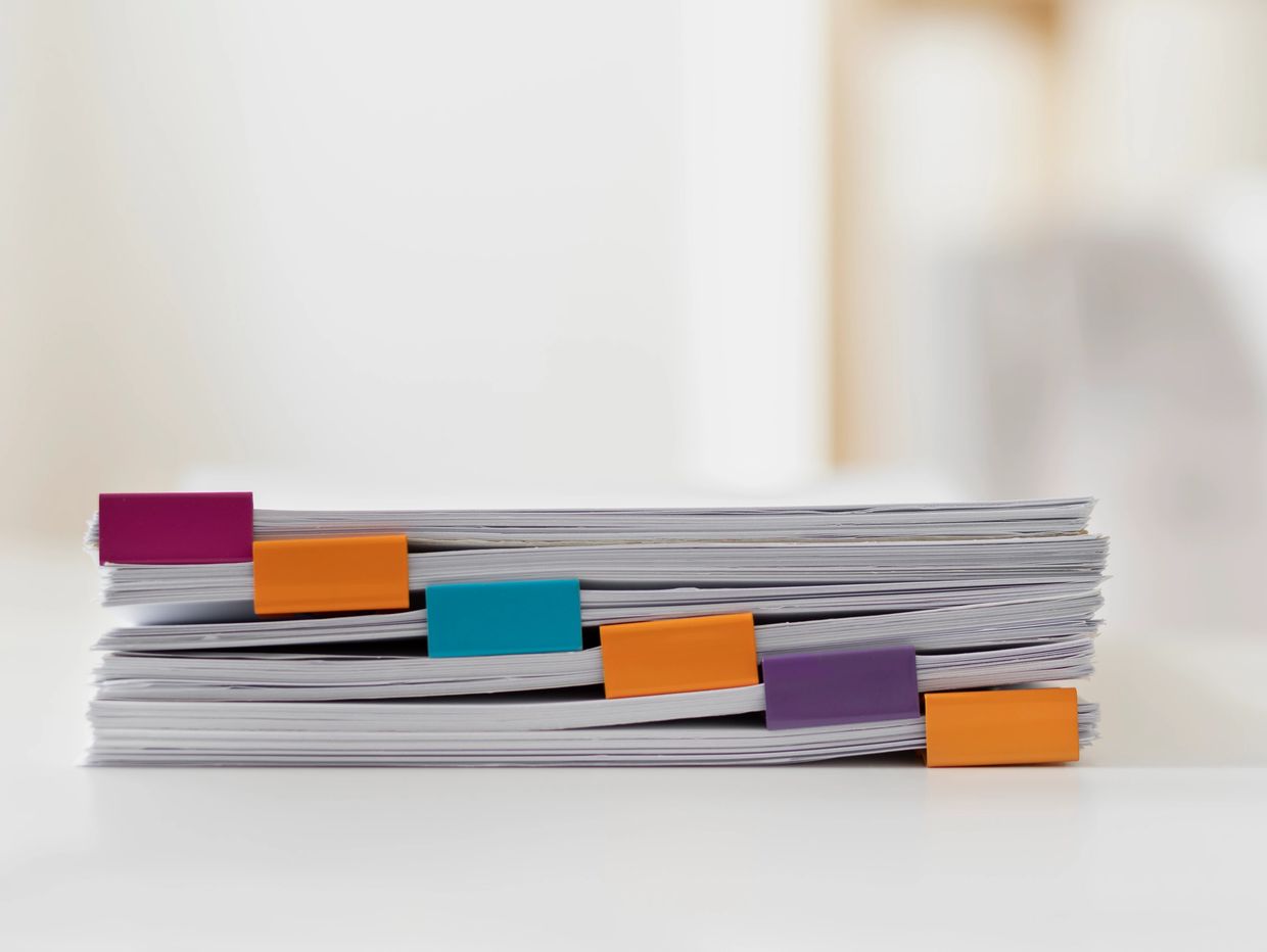 Stack of papers clipped with colorful binder clips on a white surface.