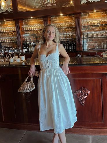 Woman in white dress posing at a winery bar.