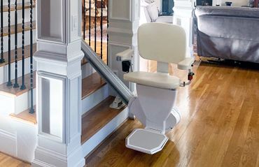 A beige stairlift installed on a wooden staircase in a home.