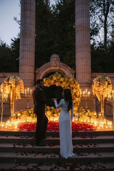 Couple exchanging vows in romantic candlelit outdoor setting.