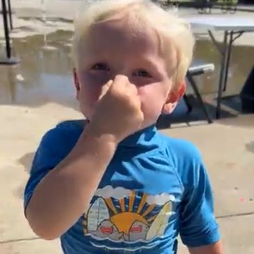 Young boy covering his nose outdoors near water.