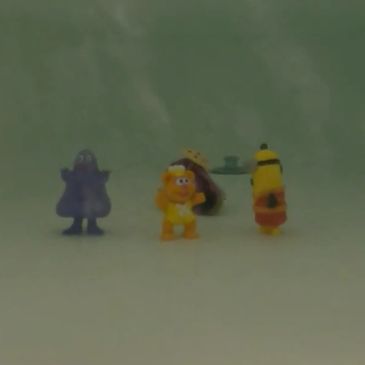 Three small colorful toys standing on a white surface.