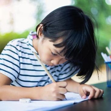 Young girl focused on writing in a notebook outdoors.