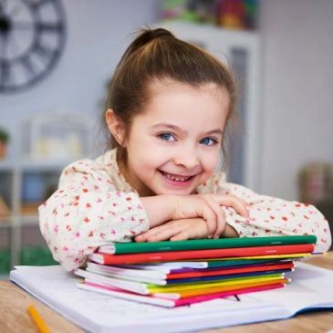 Smiling girl resting on a stack of colorful notebooks.
