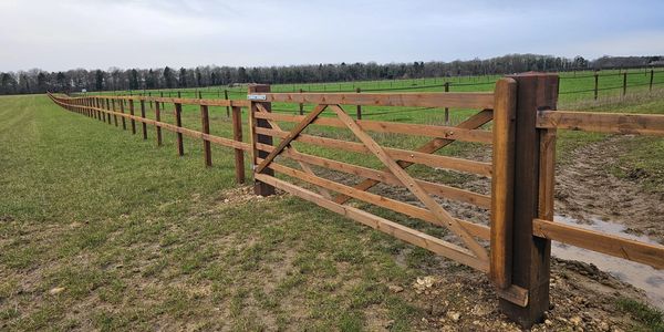 Long wooden fence gate in a grassy field.