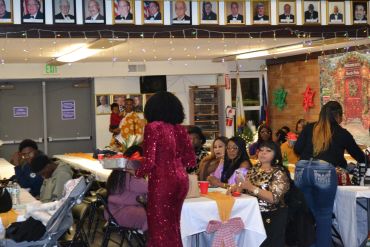 People dressed elegantly enjoying an indoor celebration with decorations and framed photos.