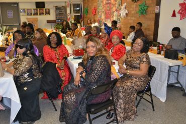 Group of women in elegant dresses seated at decorated tables during a festive event.