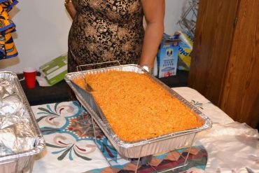 A large tray of cooked rice on a table, with a person standing behind it.