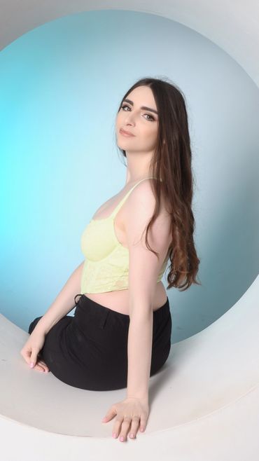 Young woman with long hair in a yellow top and black skirt poses gracefully.
