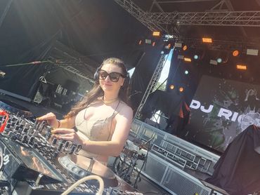 Female DJ performing on stage with headphones and DJ equipment.