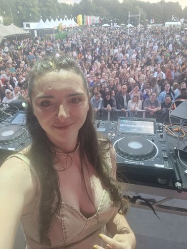 DJ taking a selfie with a large crowd at an outdoor music festival.