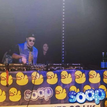 DJ performing with a duck-themed Soop banner in a dimly lit venue.