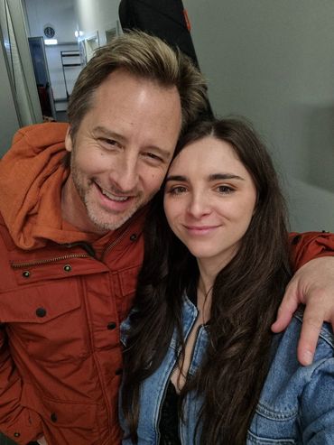 Two people smiling warmly for a close-up selfie indoors.