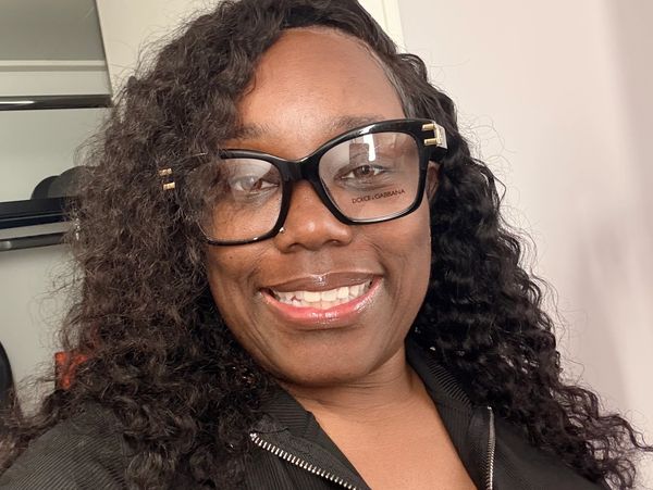 Woman smiling with large glasses and curly hair.