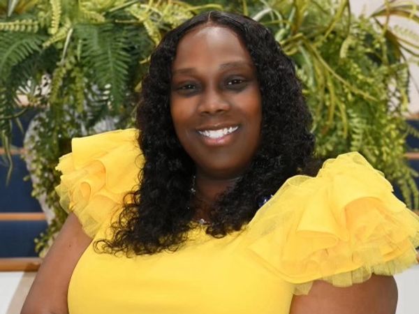 Woman smiling in a yellow top with ruffled sleeves.