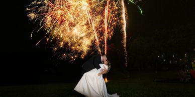 Newlyweds share a romantic kiss with fireworks lighting up the night sky.