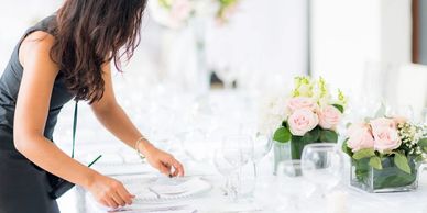 Woman arranging table settings at a floral-decorated event.