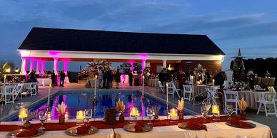 Elegant outdoor evening event by the pool with candlelit tables and soft purple lighting.