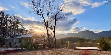 Sunset behind trees and mountains near a house.