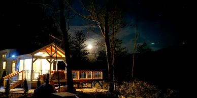 House lit up at night with moon and trees.