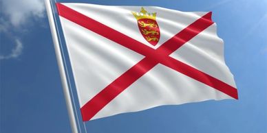 Flag with red diagonal cross and crowned emblem against blue sky.
