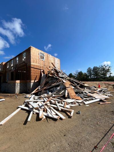 Debris and construction materials piled beside a partially built wooden house under a clear blue sky.