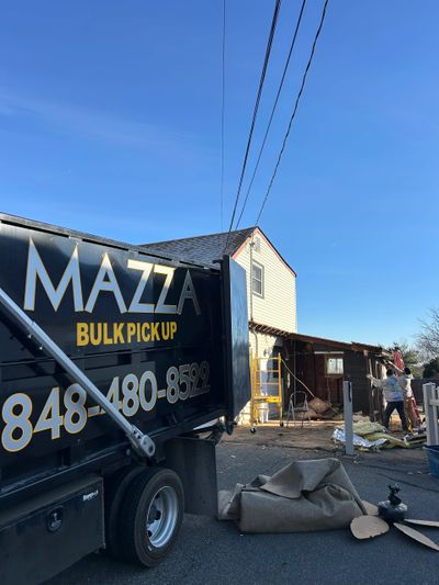 MAZZA bulk pickup truck at a house with workers cleaning up debris.